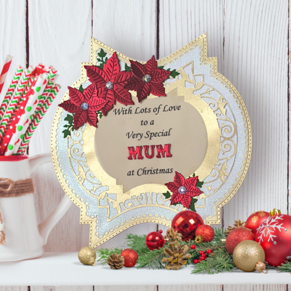 Gorgeous shaped card with decorative layers, personalised message and handcrafted poinsettias Christmas card displayed on a white shelf in front of a white panelled wall with Christmas decorations.