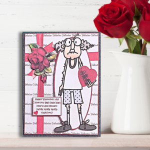 Grumpy Gus Yada Yada Yada Valentine's Card displayed on a Wooden shelf wth a vase of red roses in front of a white painted brick wall