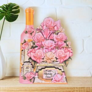 A fully shaped, multi layered rose bouquet and bottle of wine card is shown displayed on a wooden shelf in front of a white wall.