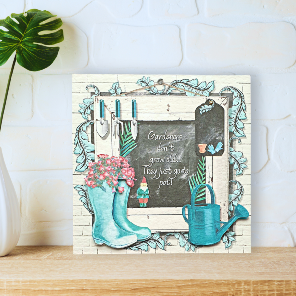 Green Potting Shed Wellies and watering can in front of a blackboard card displayed on a a wooden shelf in front of a white wall.