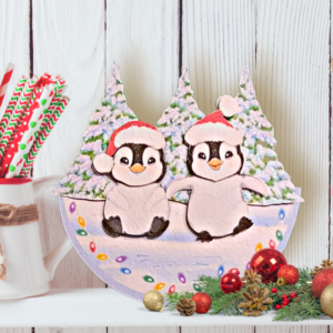 Festive Cuties penguin rocker card displayed on a white shelf next to a mug of candy canes