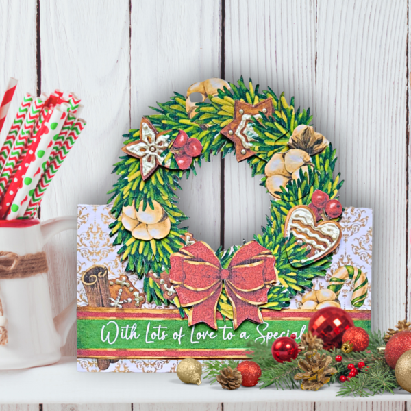 A white shelf in front of a white panel wall with a wreath shaped Christmas card. The wreath is decorated with a red bow and gingerbread.