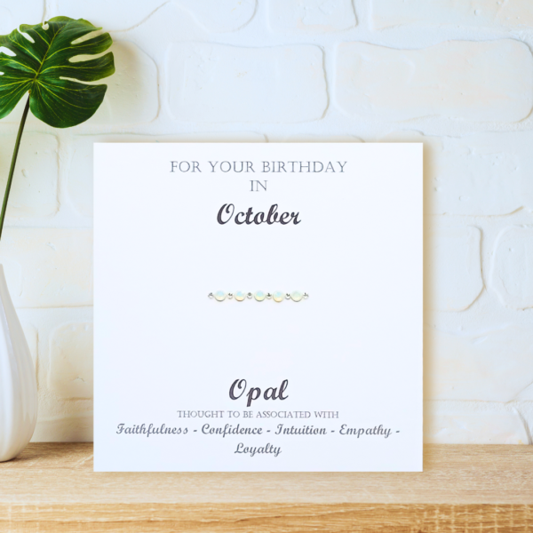 Opal October Birthstone - card displayed on a wooden shelf in front of a white wall.