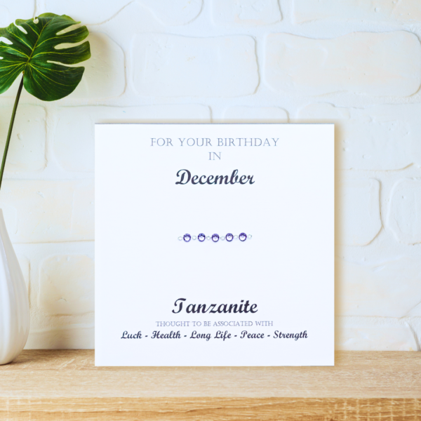 Tanzanite - December Birthstone card displayed on a wooden shelf in front of a white wall.