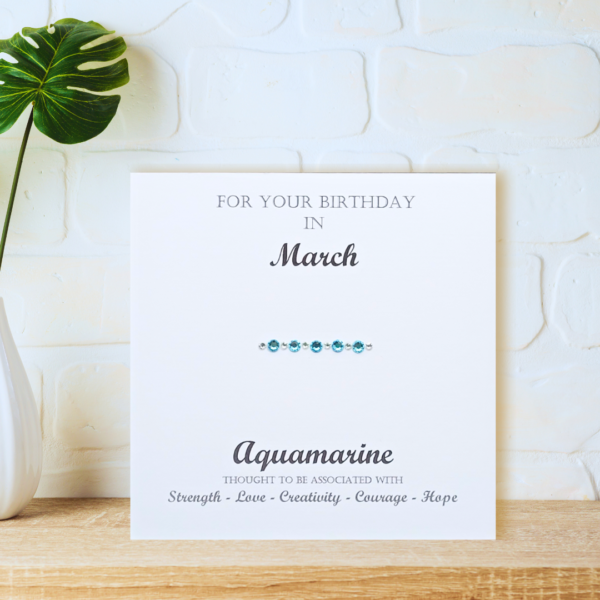 Aquamarine March Birthstone card displayed on a wooden shelf in front of a white wall.