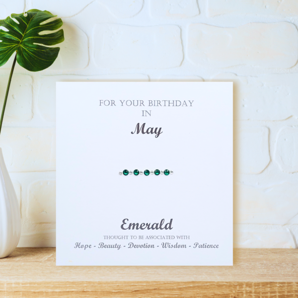 Emerald May Birthstone - card displayed on a wooden shelf in front of a white wall.