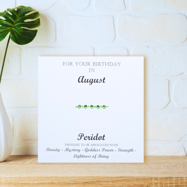 Peridot August Birthstone card displayed on a wooden shelf in front of a white wall.