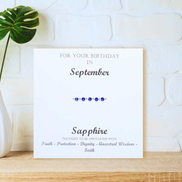 Sapphire September Birthstone card displayed on a wooden shelf in front of a white wall.